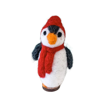 Knitted penguin with a red scarf and hat on a white surface with a light blue background